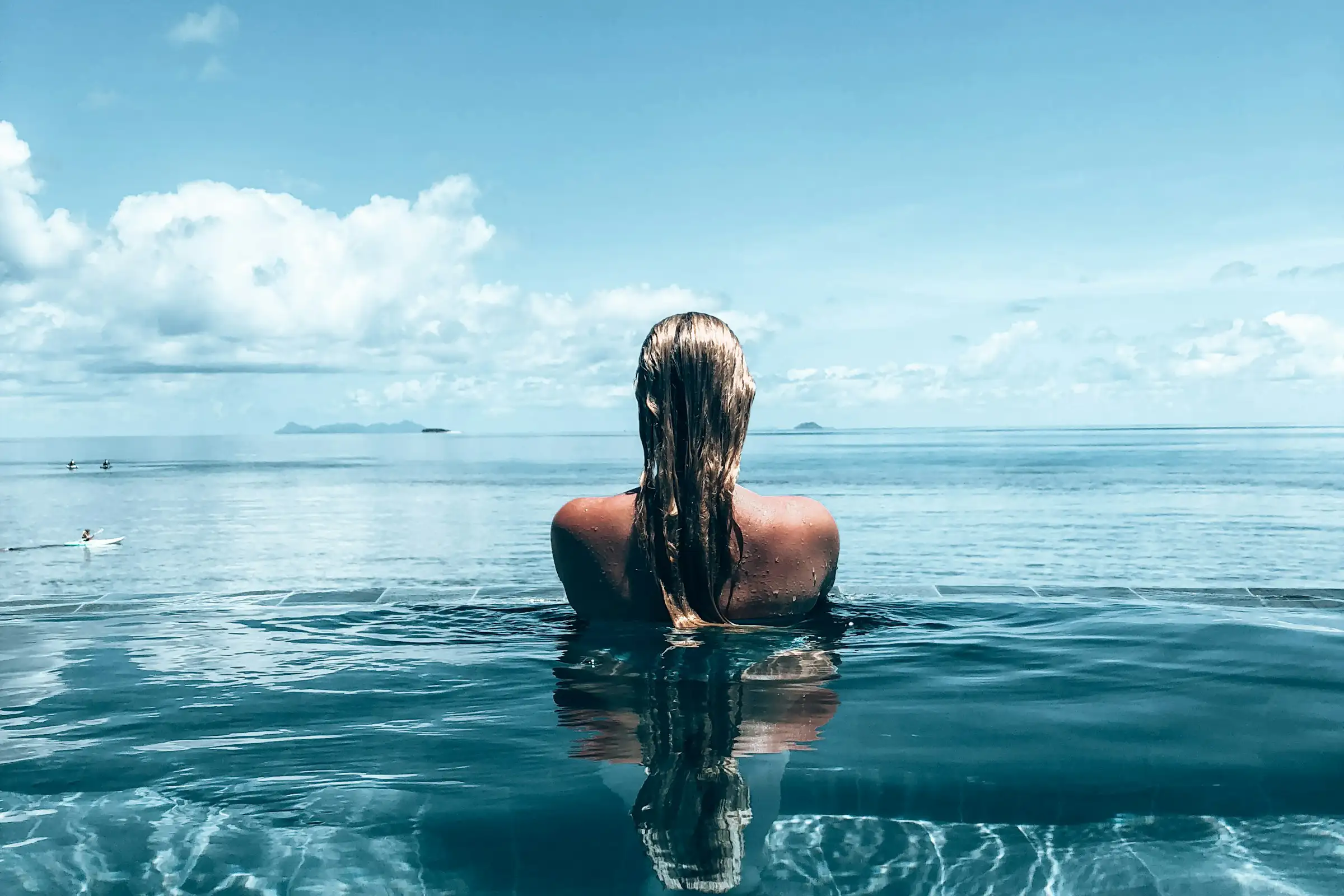 A woman in an infinity pool stares out at the ocean