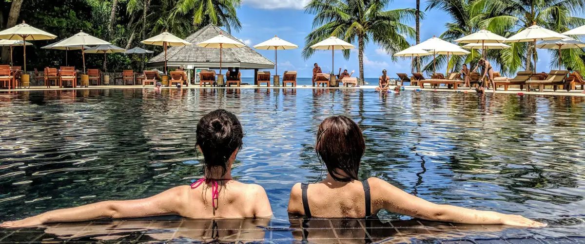 two women sitting in a pool overlooking a beautiful tropical beach